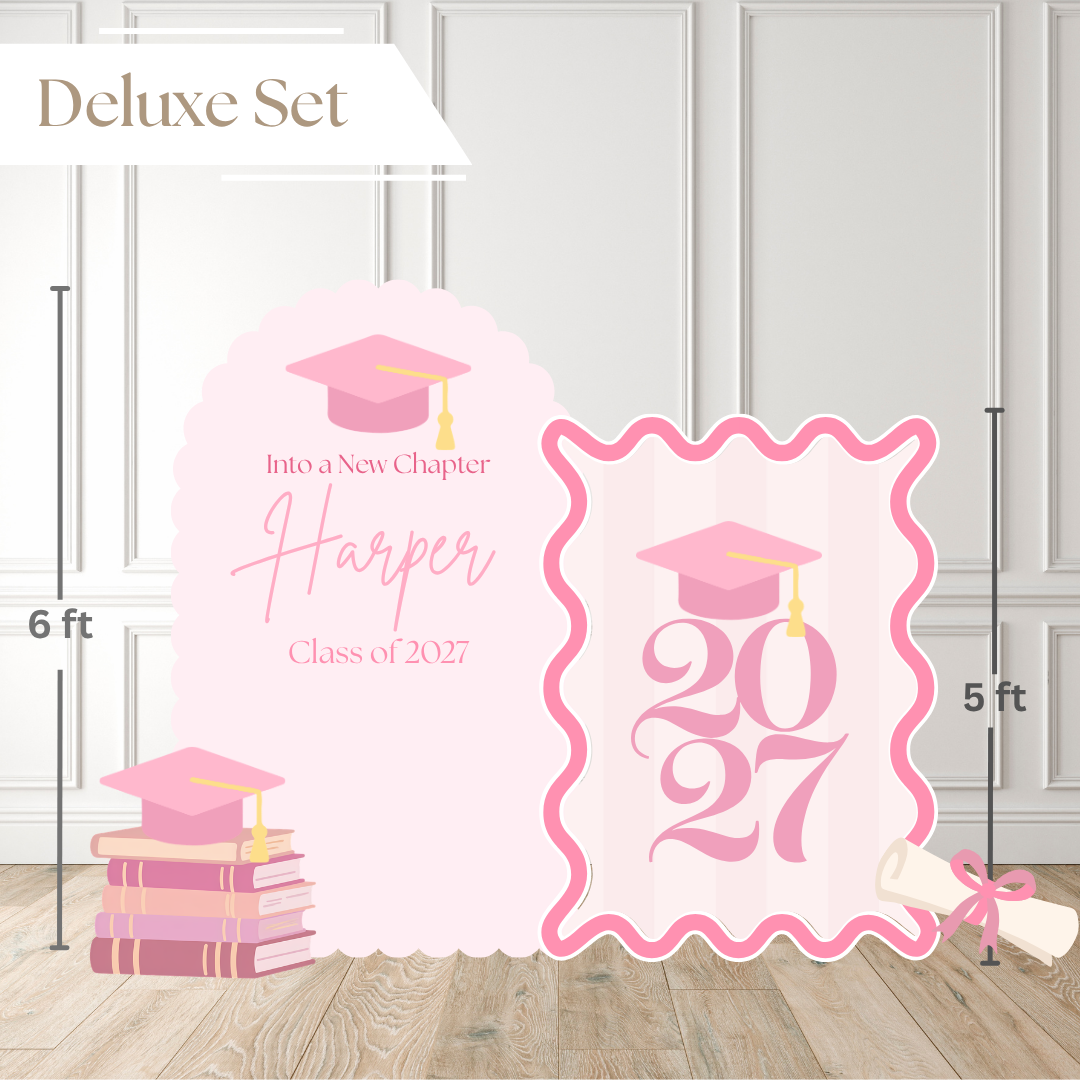 Pink graduation party backdrop set labeled 'Deluxe Set' with two freestanding panels, one arched and one scalloped, featuring a graduation cap, books, a rolled diploma, and customizable text including 'Harper' and 'Class of 2027'. Measurement lines indicate 6 ft tall and 5 ft wide, with a light paneled wall and wood floor background.