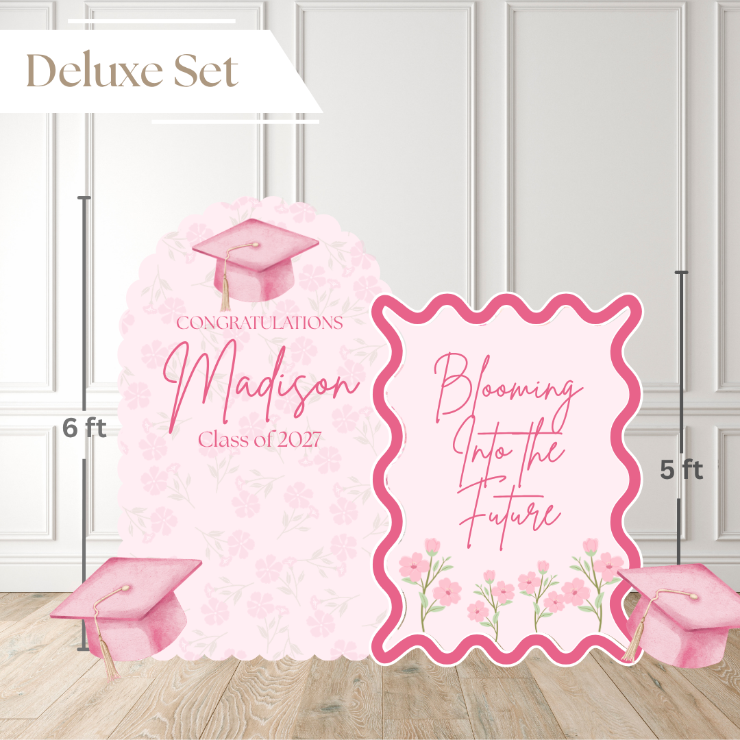 Pink graduation backdrop set with two decorative panels reading 'Congratulations Madison Class of 2027' and 'Blooming Into the Future,' plus pink graduation caps and flowers, shown with height markings on a white paneled wall and wood floor.