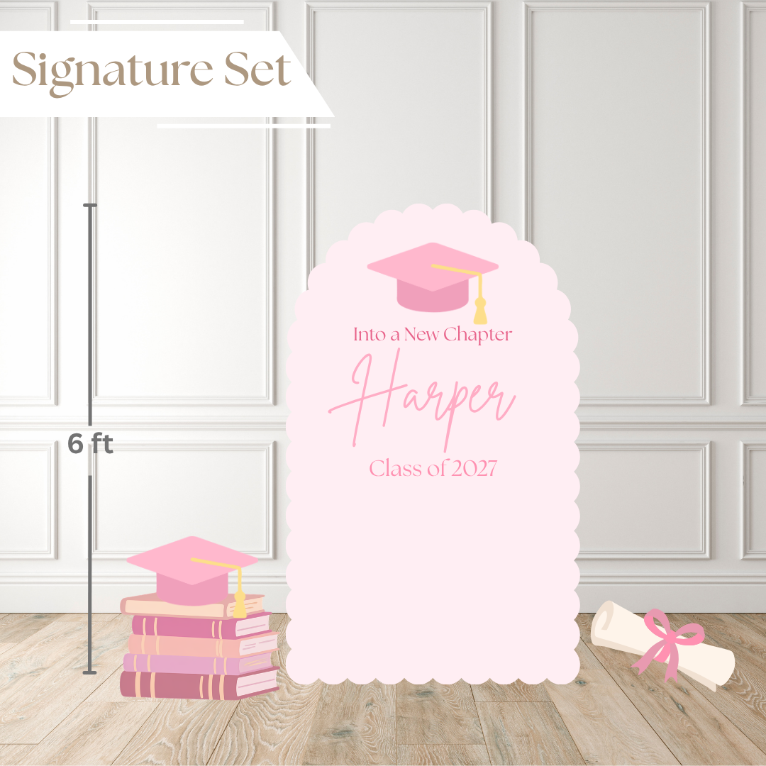 Pink graduation-themed party backdrop set with a large scalloped arch sign reading 'Harper Class of 2027', a stack of pink books, a diploma scroll, and a white banner that says 'Signature Set'. The scene is staged against white paneled walls on a wood floor, with a height marker indicating 6 ft.